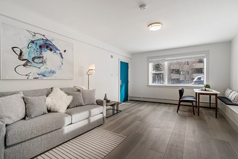 A living room with a grey couch and a painting on the wall.